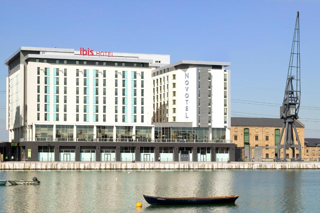 O ibis London Excel-Docklands na beira do rio, com quatorze andares e o nome em destaque em vermelho, para representar hotéis Ibis em Londres