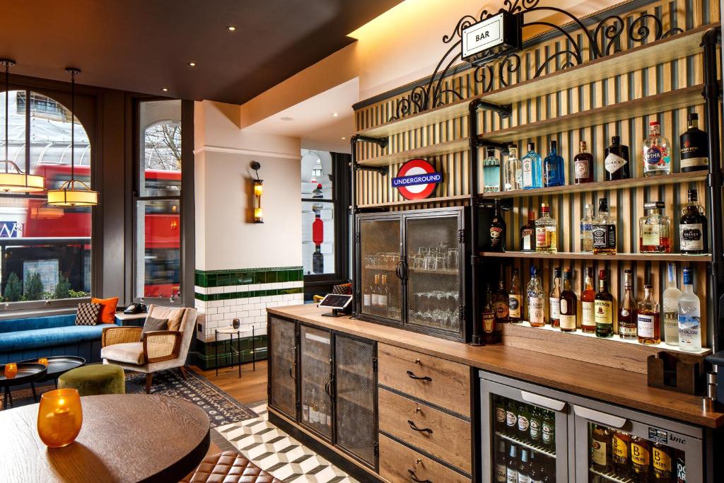 Bar do ibis Styles London Gloucester Road em um ambiente compartilhado com diversas opções de bebida, poltronas e sofás com uma janela ampla dando vista para a rua