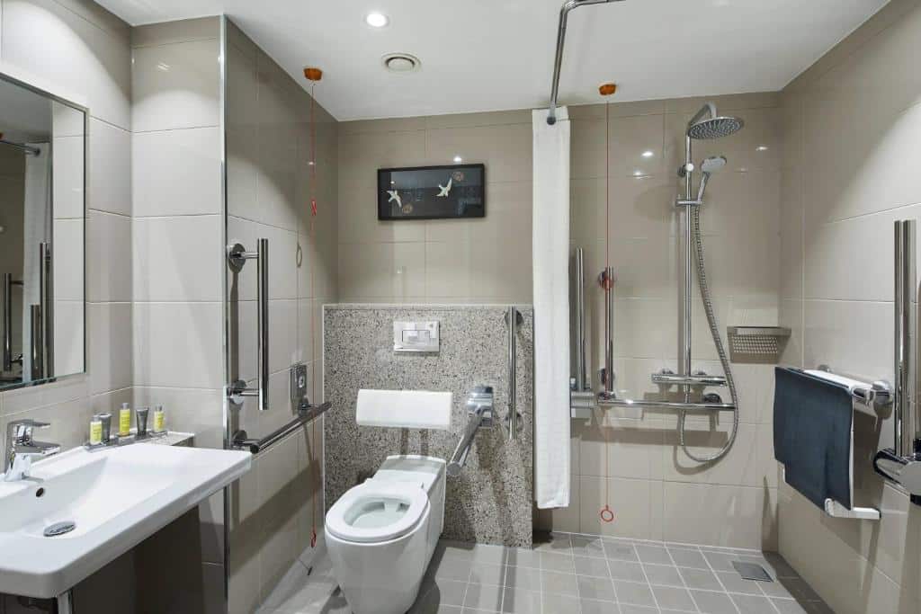 Banheiro adaptado do London Heathrow Marriott Hotel com barras de apoio, cordão de emergência e outros recursos úteis para pessoas com deficiência