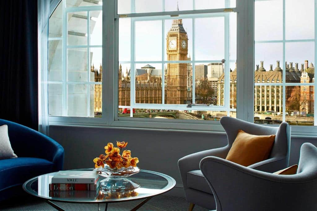 Uma janela ampla do London Marriott Hotel County Hall com vista para o Big Ben, há duas poltronas, uma mesinha de centro e um vaso de flor