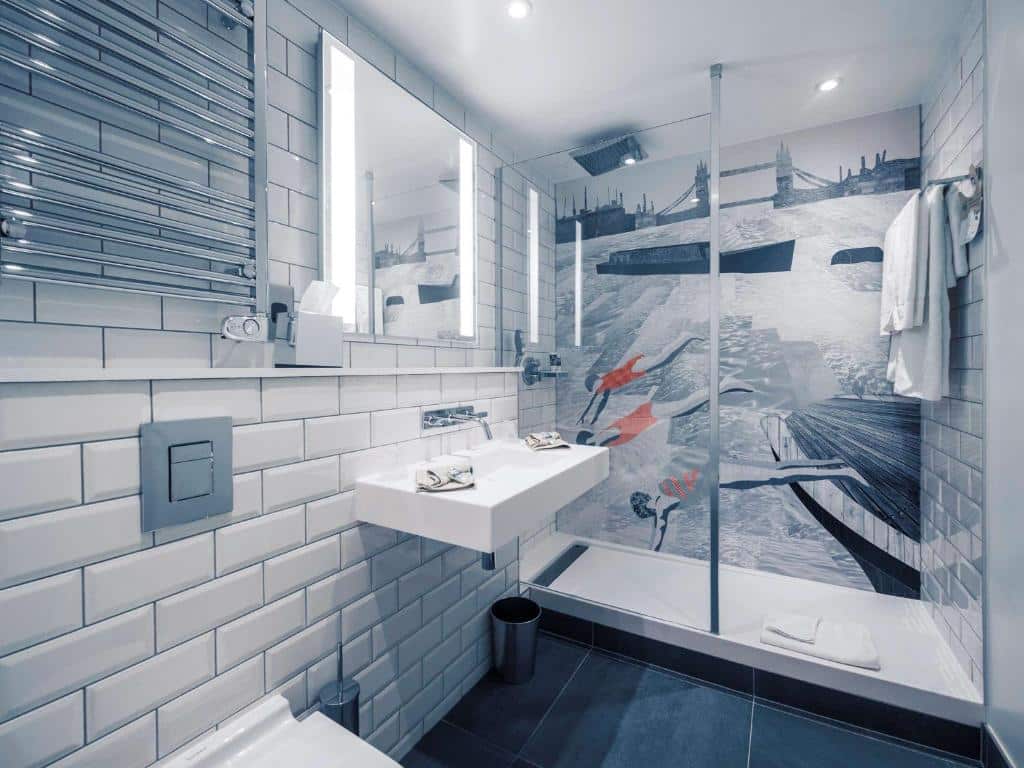 Banheiro do Mercure London Bridge com um box amplo, uma pia, um espelho e algumas toalhas espalhadas pelo ambiente, para representar hotéis em Londres para brasileiros