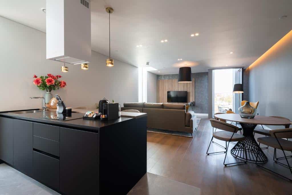 Sala de estar do Mirabilis Apartments - Bayham Place com uma janela ampla, um sofá, uma televisão, uma mesa redonda com quatro lugares, uma bancada de cozinha com vasos de flores e uma cafeteira