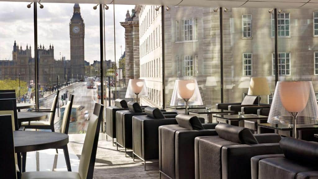 Salão de refeições do Park Plaza Westminster Bridge London com diversas mesas, poltronas, abajures e janelas panorâmicas com vista para o Big Ben