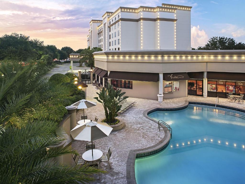 piscina com bordas sinuosas e a estrutura do Buena Vista Suites Orlando, um dos hotéis para brasileiros em Orlando, atrás com várias luzes redondas ao redor das bordas da estrutura
