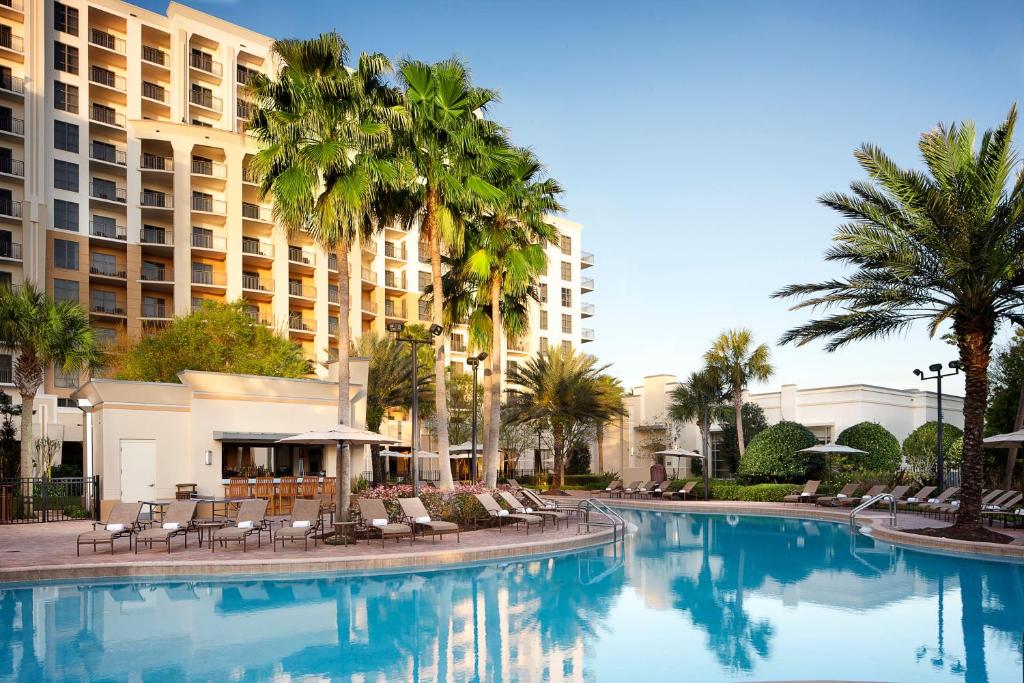 piscina com bordas arredondadas com cadeiras e palmeiras em frente à fachada do Hilton Grand Vacations Club Las Palmeras Orlando, uma das opções na International Drive em Orlando