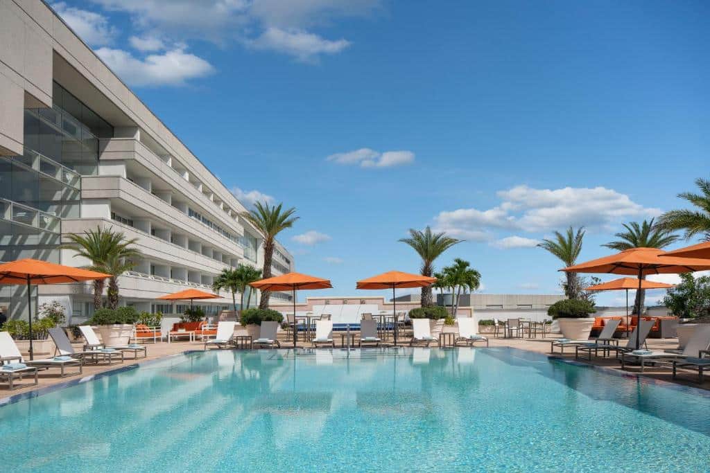 piscina ao ar livre no terraço do Hyatt Regency Orlando International Airport Hotel, um dos hotéis de luxo em Orlando, com palmeiras, espreguiçadeiras e a estrutura moderna do hotel ao lado