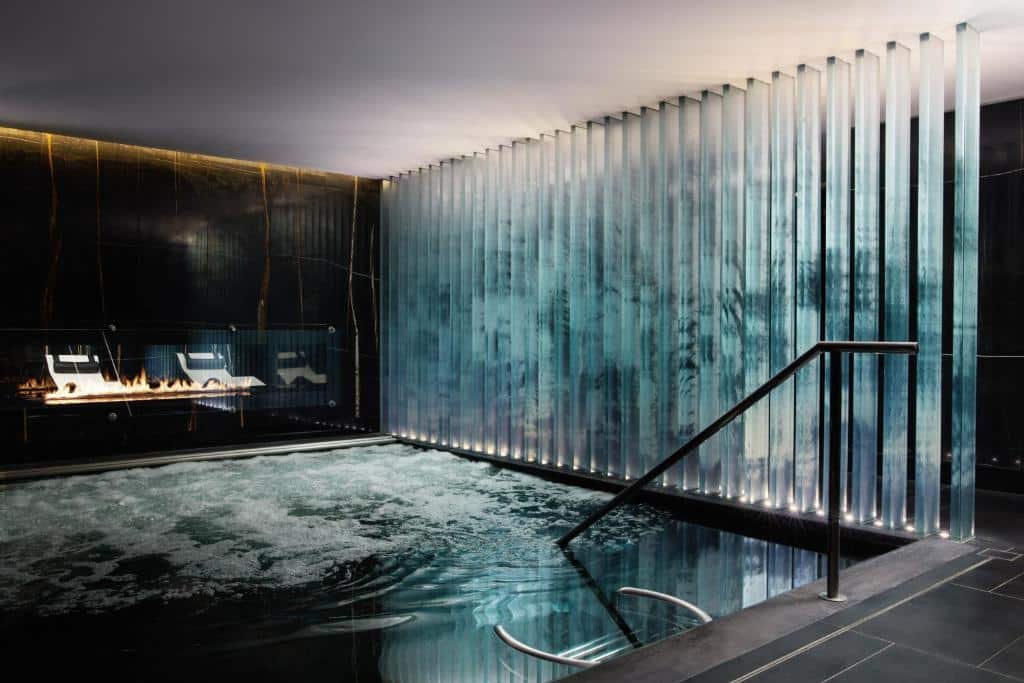 Piscina coberta do Corinthia London com uma escada e colunas acrílicas que refletem a corda da água, para representar hotéis perto do Big Ben em Londres