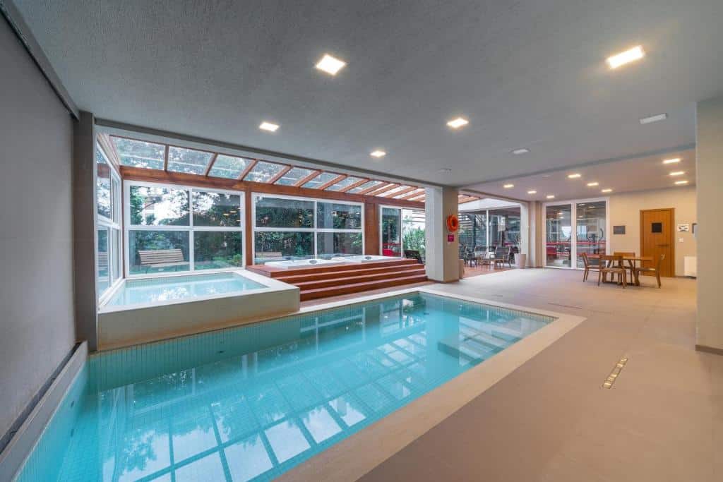 piscina coberta do Hotel Laghetto Stilo Borges com duas banheira de hidromassagem e uma mesa de madeira com quatro lugares próximo à beirada.