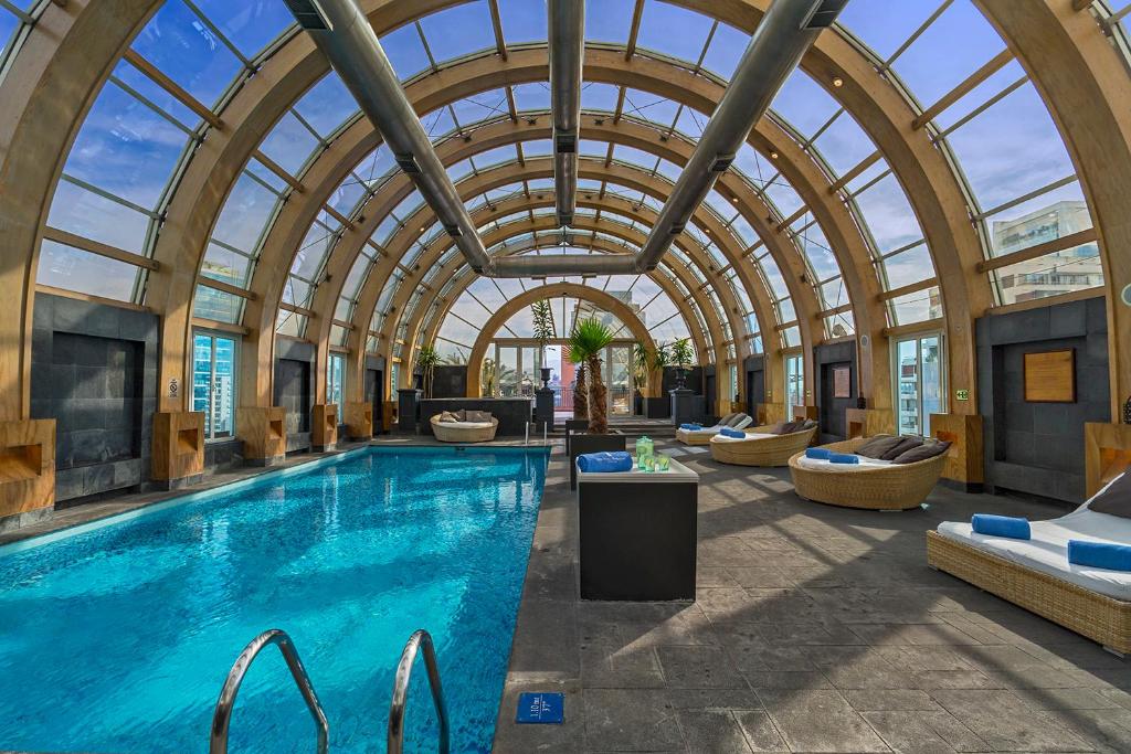 Piscina coberta do The Ritz-Carlton,  piscina do lado esquerdo com poltronas redondas do lado direito. Representa hotéis perto do aeroporto de Santiago.