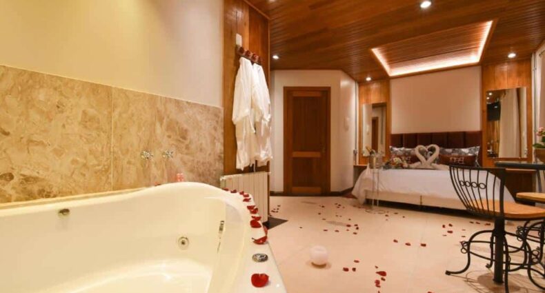 quarto da pousada boro em Gramado mostrando uma banheira de hidromassagem no canto inferior esquerdo e uma cama de casal com toalhas e formato de cisnes em cima, no canto superior direito