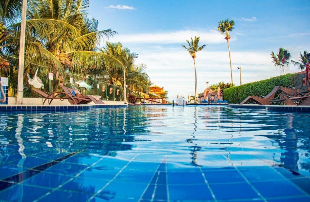 Piscina da Pousada Polymar, uma das opções de hotéis em Maragogi, aparendo a  água da piscina, espreguiçadeiras e árvores em volta
