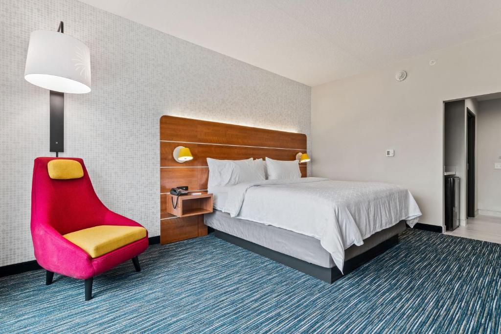 quarto amplo com poltrona vermelha e cama de casal com mesinha e luminária de ambos os lados do Holiday Inn Express & Suites Orlando- Lake Buena Vista