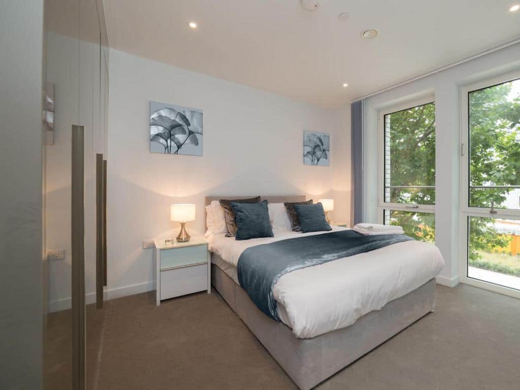Quarto do Deluxe Central London Apartment com uma cama de casal, um armário e duas janelas amplas, há duas mesinhas de cabeceira com abajures