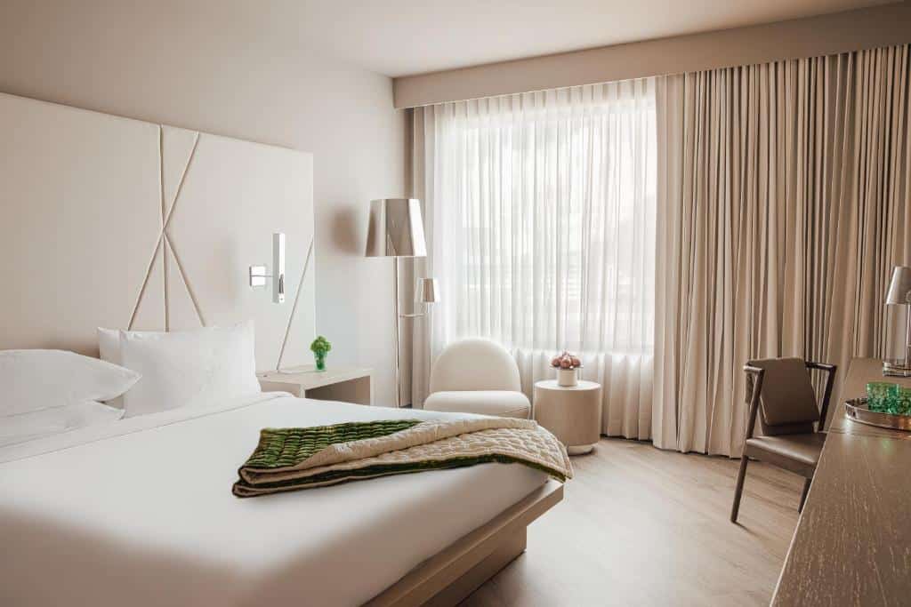 quarto do ette luxury hotel & spa, em Orlando, com decoração minimalista toda em branco, móveis arredondados e acolchoados, mesinha e luminário de ambos os lados, sofás e janela grande