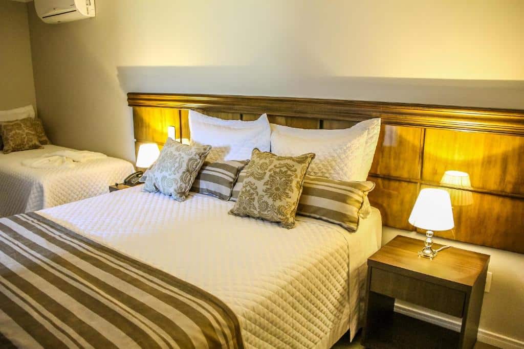 suíte do Hotel Gramado Interlaken com uma cama de casal e uma de solteiro no canto superior esquerdo. As camas estão cobertas com lençóis em tons bege e dourados.