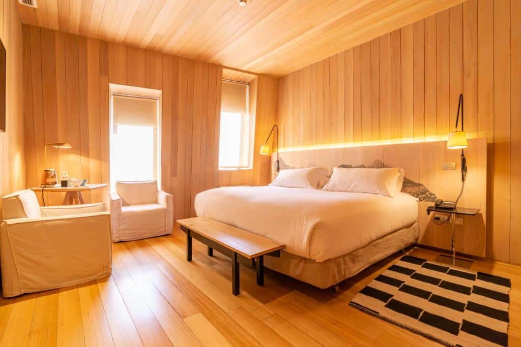 Quarto do Hotel Magnolia com cama de casal no lado direito com duas luminárias a frente, duas poltronas em frente a cama.