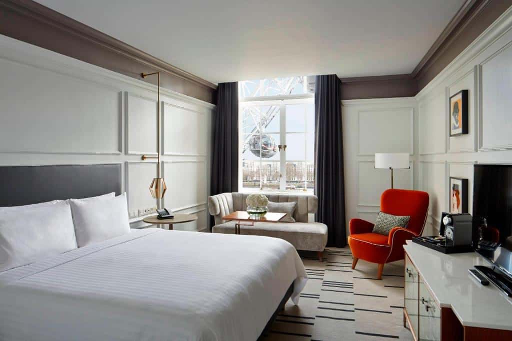 Quarto do London Marriott Hotel County Hall com uma cama de casal, uma sofá, uma poltrona, carpete, uma janela com vista direta para a London Eye, para representar hotéis bem localizados em Londres