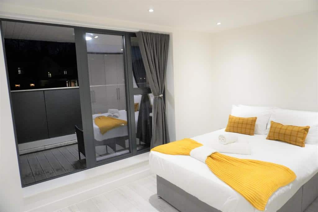 Quarto do Queens Luxury Apartments com uma sacada com cortinas, uma cama de casal com toalhas e almofadas sob à cama, para representar airbnb em Londres