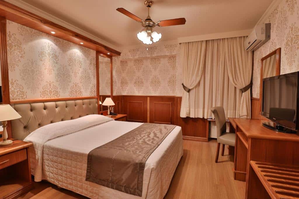 suíte do Serrazul Hotel Distributed By Intercity em Gramado com uma cama de casal no lado esquerdo e uma mesa longa de madeira com espaço para trabalhar e uma televisão em frente a cama