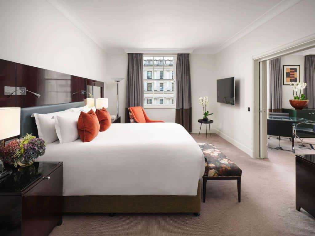 Quarto do Sofitel London St James com uma janela com cortinas, uma cama de casal, uma televisão, um carpete, uma poltrona e um segundo ambiente com uma sala de estar