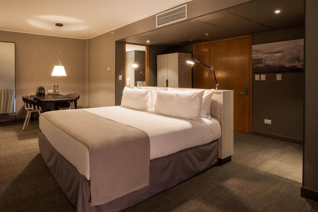 Quarto do Solace Hotel, com cama de casal no centro do quarto do lado esquerdo mesa com duas cadeiras.