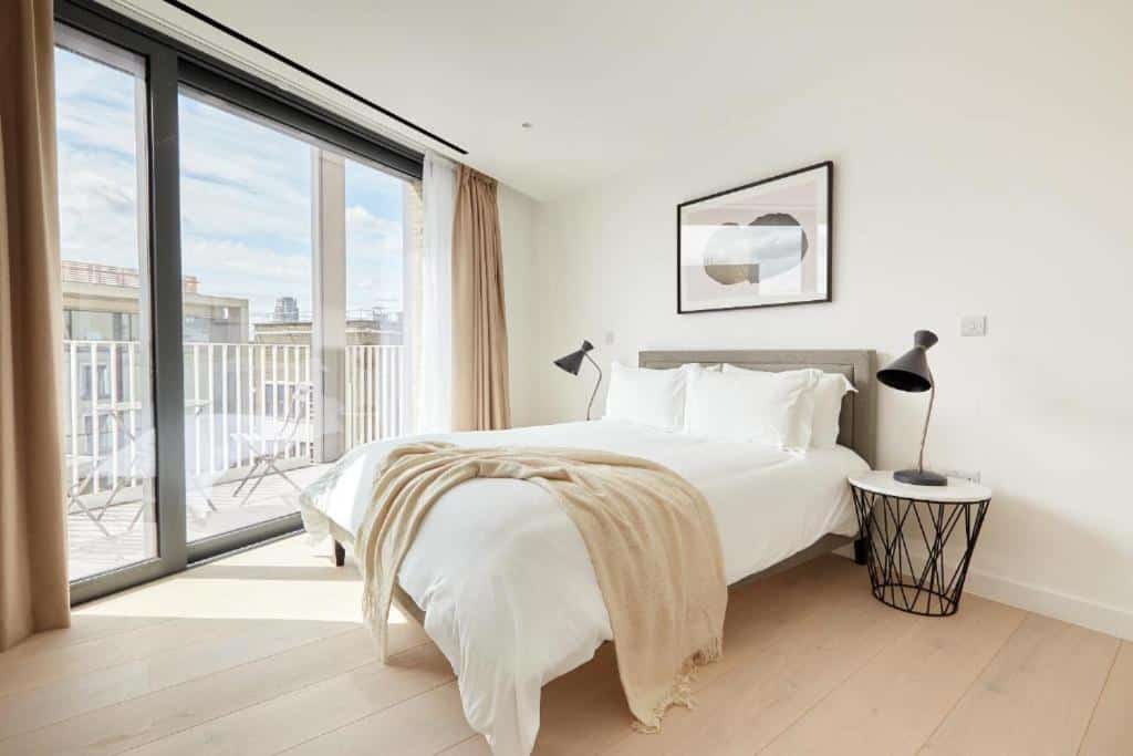 Quarto do Southwark by Q Apartments com uma sacada com cadeiras, uma cama de casal, duas cabeceiras orgânicas com luminárias, um quadro e o chão é de madeira