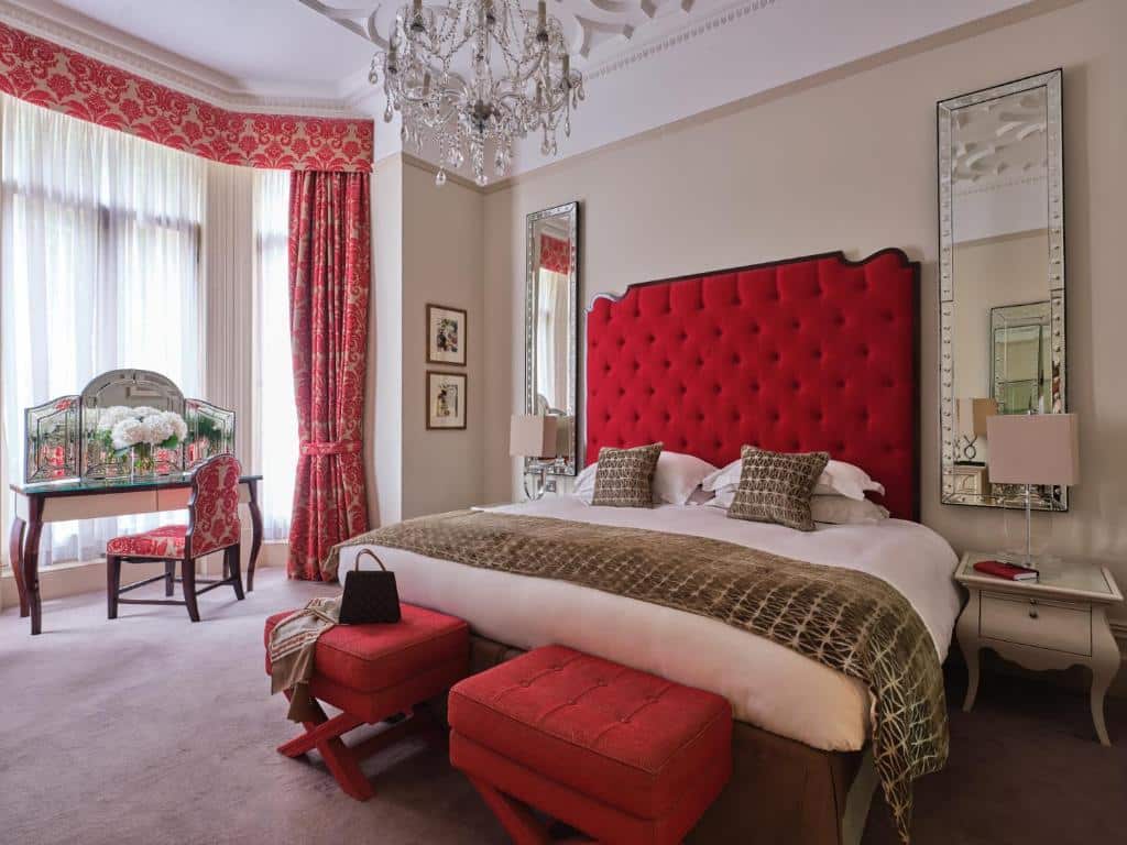 Quarto de luxo do The Apartments by The Sloane Club com uma cama de casal grande, dois espelhos, um lustre no teto, uma penteadeira e uma janela bem ampla com cortinas