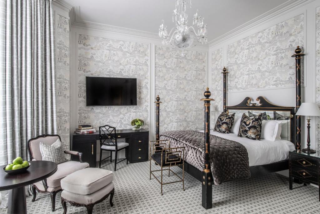 QUarto do The Kensington Hotel com papéis de parede, uma mesa de escritório com uma cadeira, uma televisão, um lustre, e uma poltrona, o espaço é decorado em tons de branco, preto e dourado