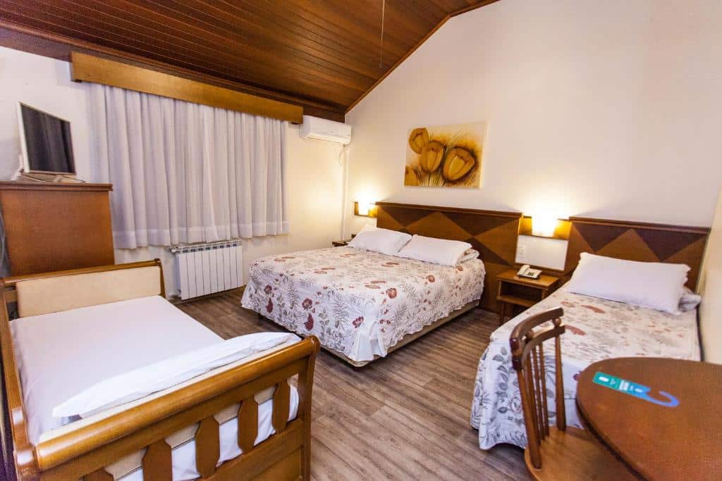 quarto do Tri Hotel Lago Gramado com uma cama de casal, uma de solteiro e um sofá cama equipados com os mesmos lençóis brancos e floridos.