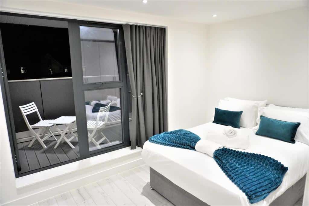 Quarto do Queens Luxury Apartments com uma cama de casal, chão de madeira clara e uma sacada com duas cadeiras e uma pequena mesa