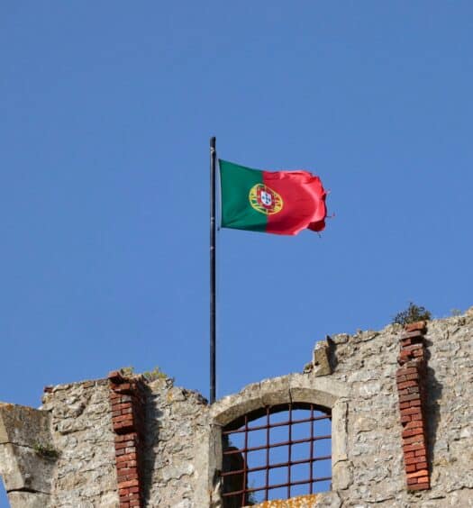 Uma bandeira de Portugal, vermelha e verde, presa ema um construção de pedras, para representar quanto custa seguro viagem Portugal