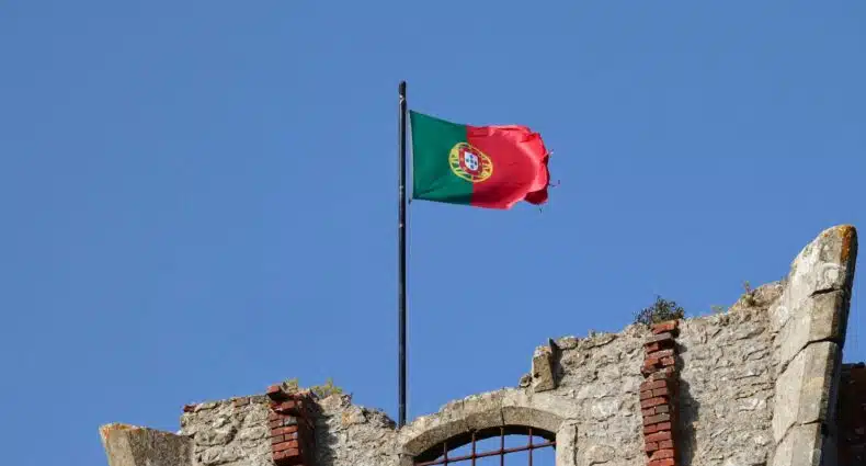 Uma bandeira de Portugal, vermelha e verde, presa ema um construção de pedras, para representar quanto custa seguro viagem Portugal