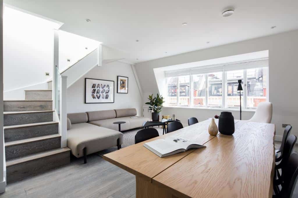 Sala do Hausd - Leicester Square com uma janela ampla, sofás, uma mesa com seis lugares e uma escada para o segundo andar, para representar airbnb em Londres