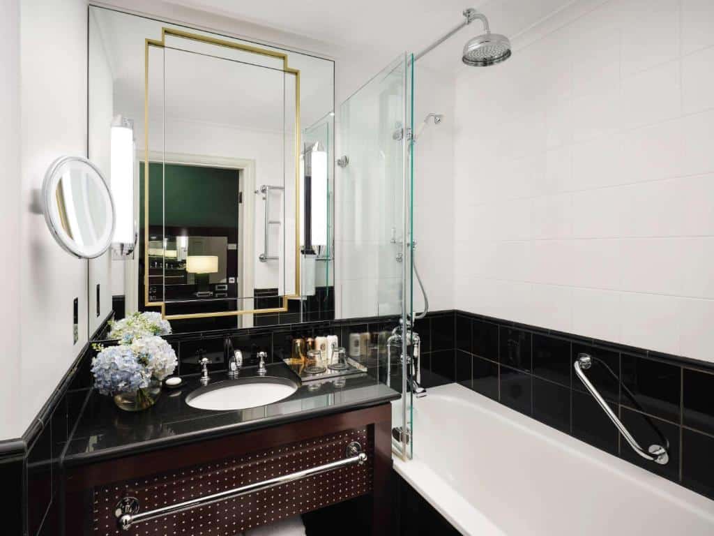 Banheiro do Sofitel London St James com uma banheira de hidromassagem, chuveiro, pia com itens de decoração e um espelho, para representar hotéis perto do Big Ben em Londres