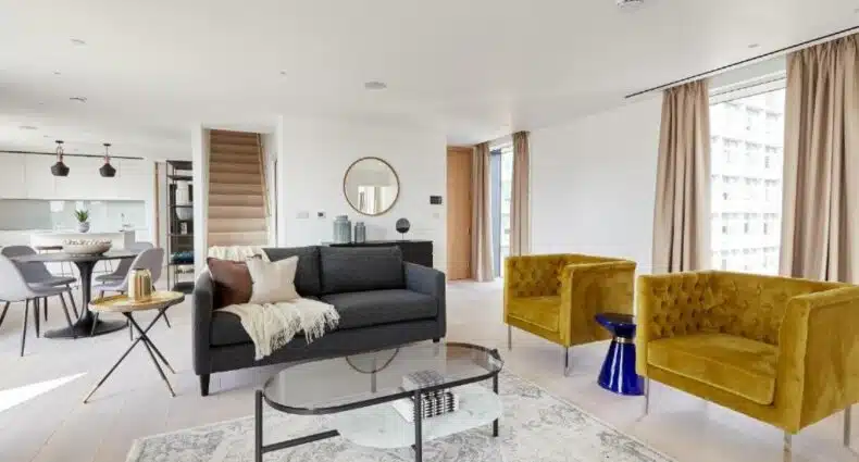 Sala de estar do Southwark by Q Apartments com duas poltronas, janelas amplas com cortinas, um sofá com dois lugares, uma mesa de centro e itens de decoração, para representar airbnb em Londres