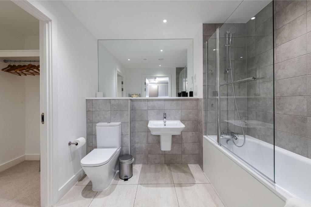Banheiro do Stayo Apartments Barking Wharf com uma banheira de hidromassagem, uma pia, um vaso sanitário e um espelho amplo, para representar airbnb em Londres
