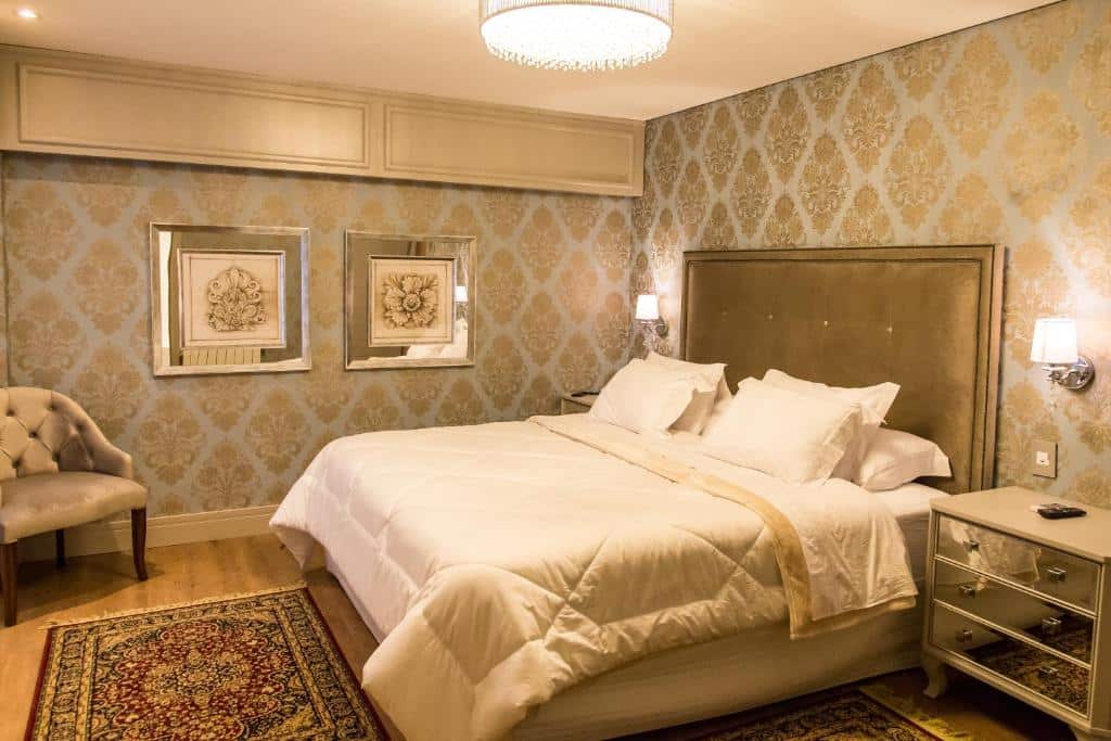 suíte do Hotel Daara em Gramado com uma cama de casal à direita, coberta de lençóis e edredom brancos, com um tapete vermelho no chão, em frente os pés da cama