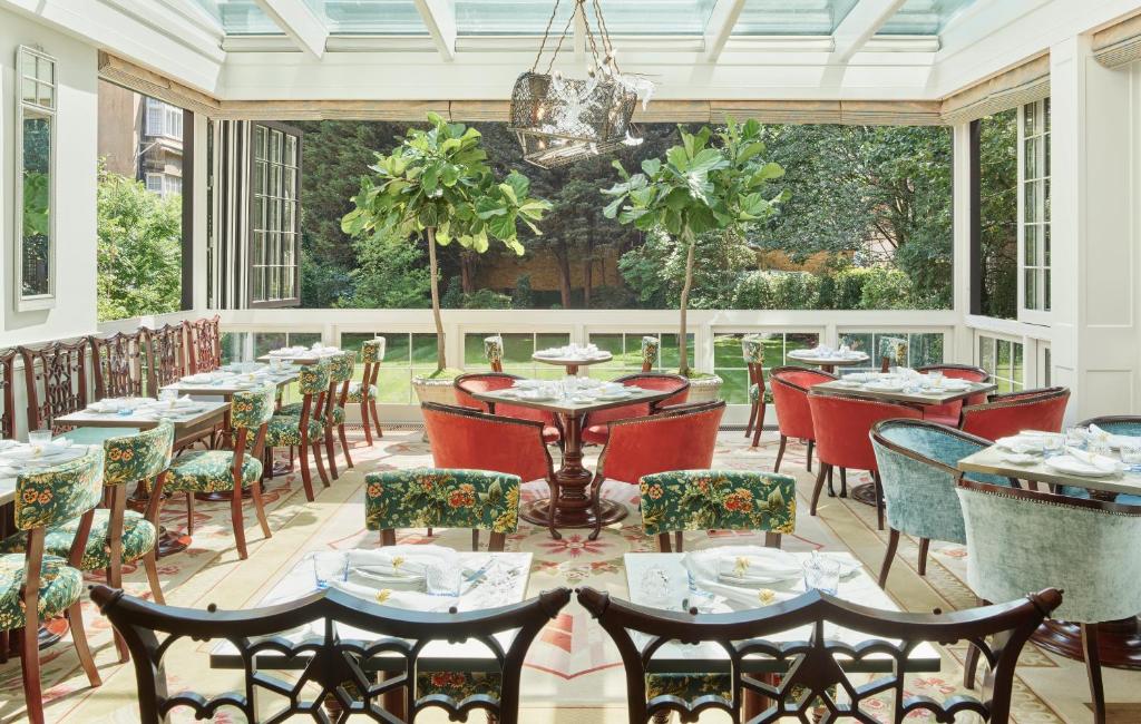 Salão aberto do The Goring com vista para um jardim, com teto de vidro e mesas quadradas com cadeiras e poltronas estofadas, para representar hotéis boutique em Londres