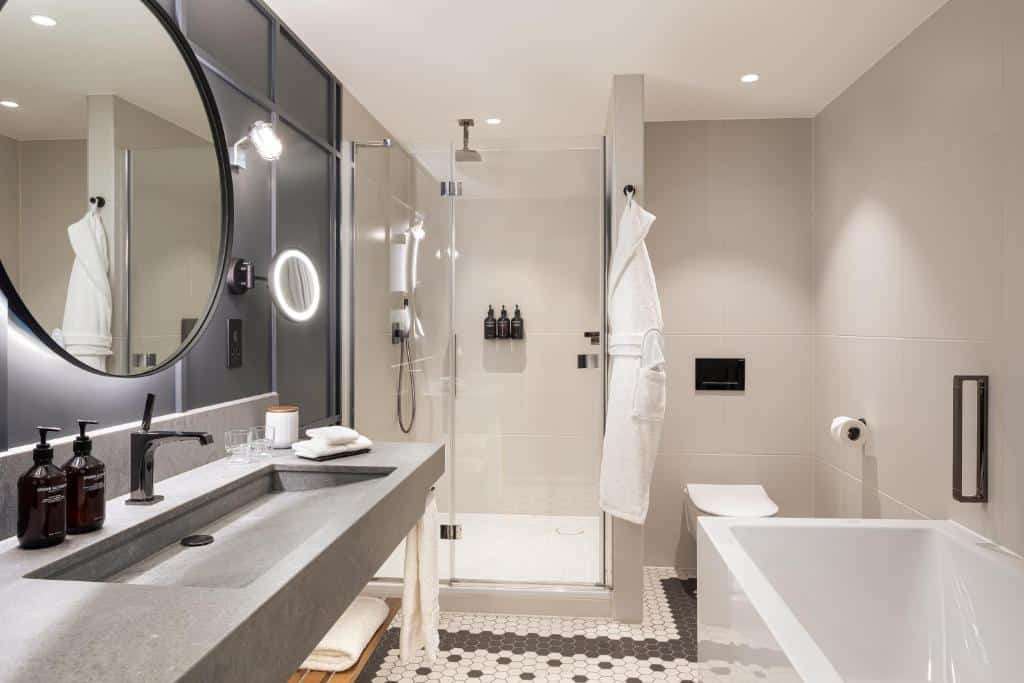 Banheiro do The Gantry London, Curio Collection By Hilton com uma banheira, um box de vidro, uma pia ampla, um espelho e itens de higiene pessoal, para representar hotéis para família em Londres