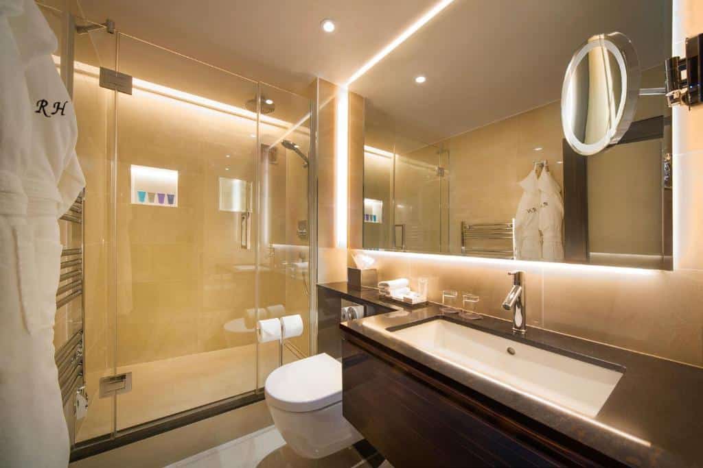 Banheiro do The Rathbone Hotel, Fitzrovia com vbox de vidro, roupões, pia ampla, vaso sanitário e um espelho amplo, para representar hotéis no centro de Londres