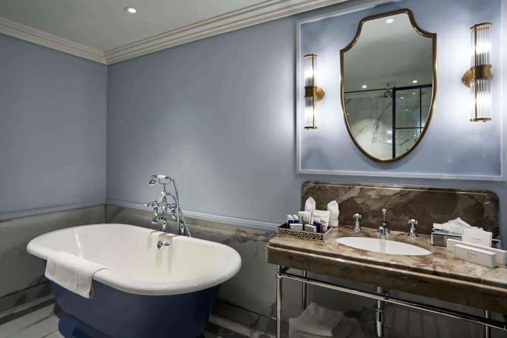 Banheiro do The Royal Horseguards com uma banheira, um espelho, uma pia com utensílios de higiene e toalhas brancas, para representar hotéis perto da London Eye em Londres