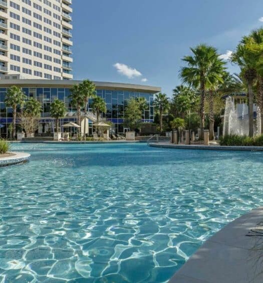piscina do Hyatt Regency Orlando, um dos hotéis de luxo em Orlando, com algumas árvores e o hotel atrás com janelas em vidro