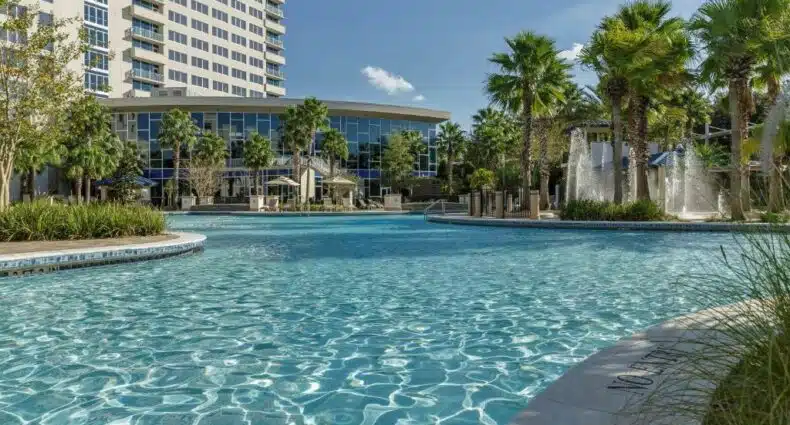 piscina do Hyatt Regency Orlando, um dos hotéis de luxo em Orlando, com algumas árvores e o hotel atrás com janelas em vidro
