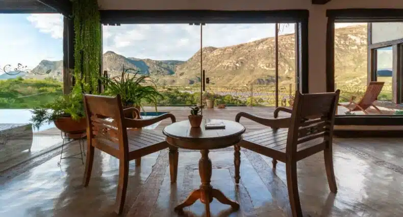 vista das montanhas no lounge compartilhado do Sítio Jatoba na Lapinha da Serra. É possível ver duas cadeiras de madeira postas lado a lado de frente para paisagem, com uma mesinha de centro também em madeira entre as duas.