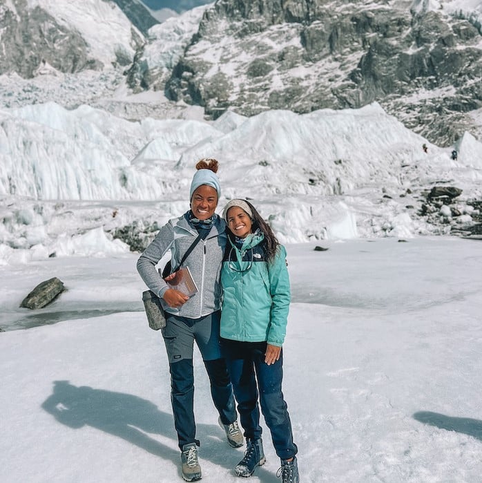 Duas mulheres abraçadas e sorrindo, num lugar que tem chão de gelo e várias montanhas de gelo ao fundo. Foto para ilustrar o post Acampamento Base do Everest