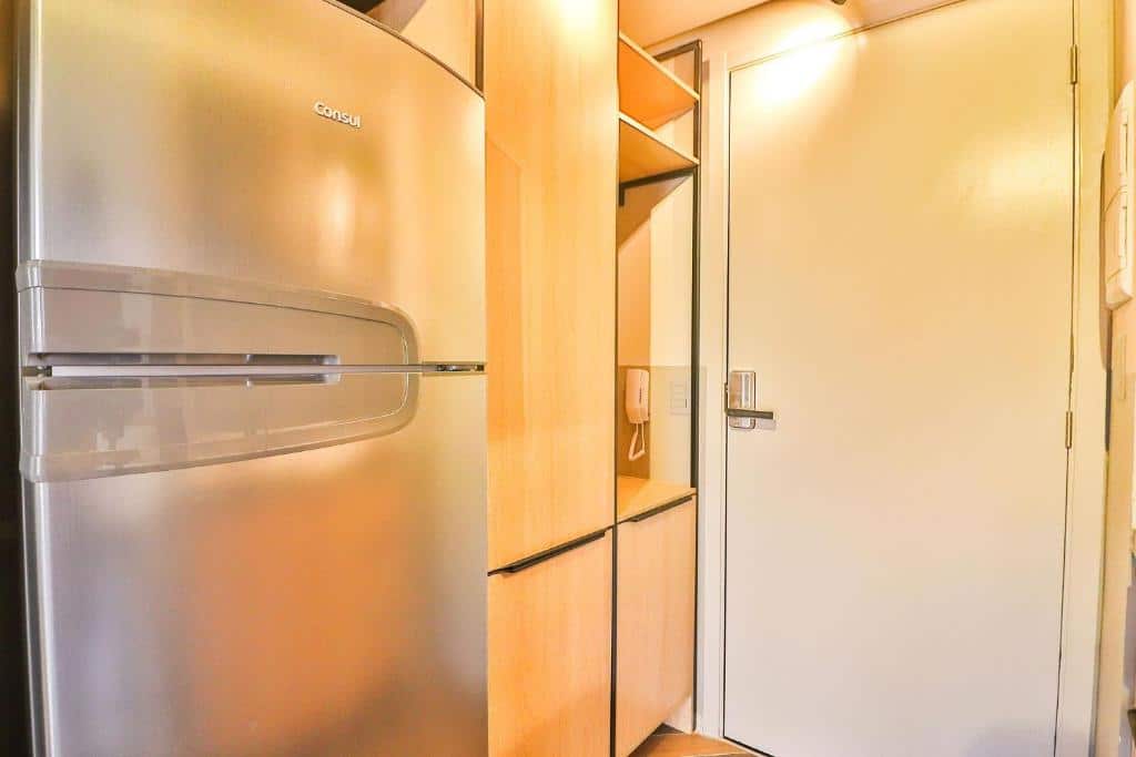 Na foto é possível ver a porta que dá aceso ao quarto do hotel e uma parte a cozinha equipada, seus armários e geladeira.