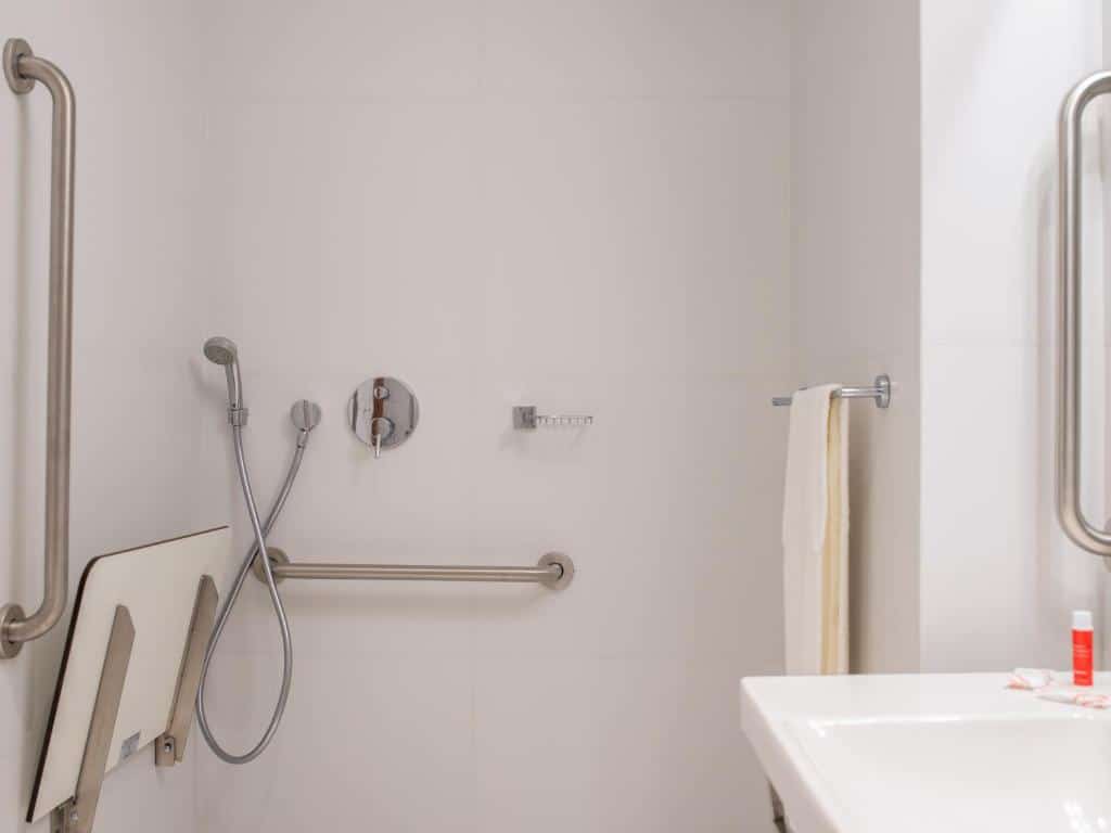Um banheiro com um chuveiro adaptado. Com várias barras na altura do quadril.