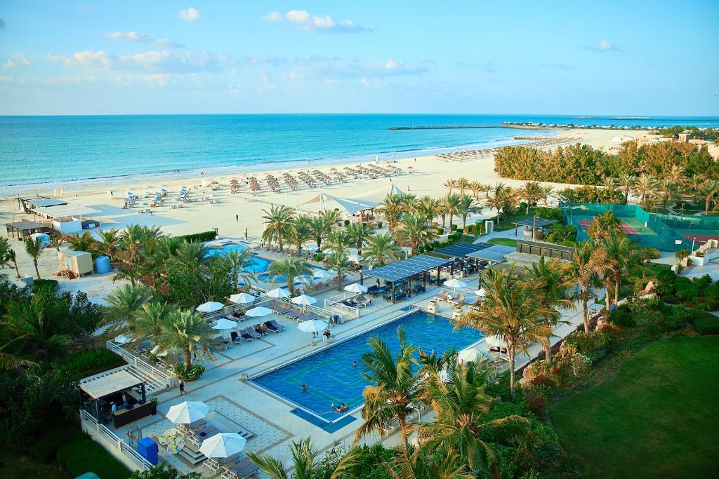 Piscinas do Al Hamra Residence de frente para a praia, cercado por palmeiras e muitos guarda-sóis e cadeiras