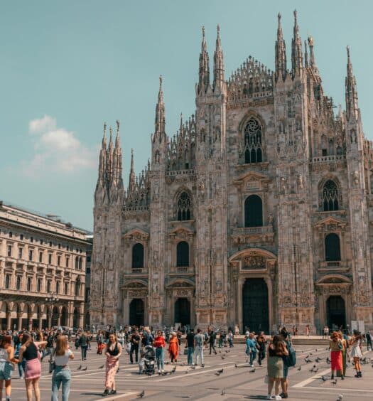 Praça em frente a Catedral de Milão com diversas pessoas andando, a catedral é construída em estilo gótico e com diversas pequenas torres