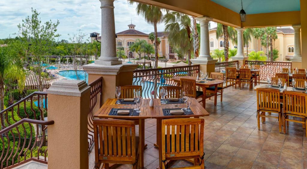 área comum com mesa e cadeiras de madeira com taças em cima e coreto com vista para a piscina abaixo, há palmeiras e a fachada atrás do Rosen Shingle Creek Universal Blvd, um dos resorts em Orlando